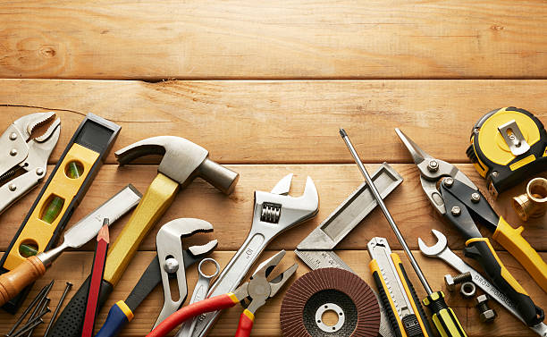 Image of tools such as hammer, wrench, pliers, and more on top of a table made of wood. 