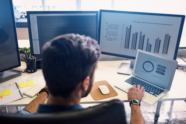 Man looking at data on laptop and computer desktop monitors