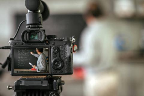 image of a video camera pointing at a blurred image of an instructor at a chalkboard