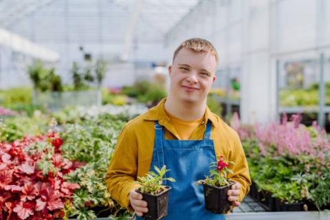 Image of a student with special needs in a greenhouse holding potted plants.