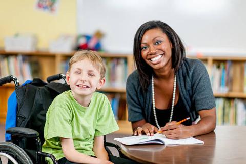 Image of teacher and young student seated in a wheelchair. Both are smiling at the camera.