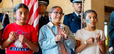 Three students with painted faces stand in front of ROTC members